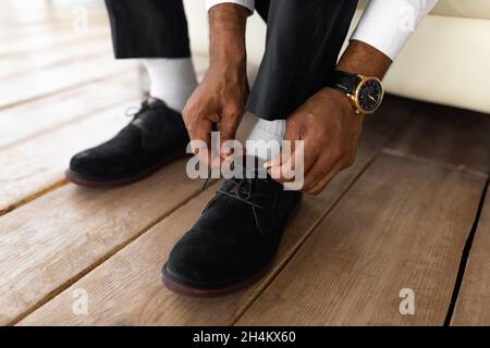 Business Und Mode. Nahaufnahme Kurzer Blick Auf Den Nicht Erkennbaren Jungen Afroamerikanischen Geschäftsmann, Der Schuhe Anlegt Und Schnürsenkel Zu Hause Bindet, Gelesen Wird Stockfoto