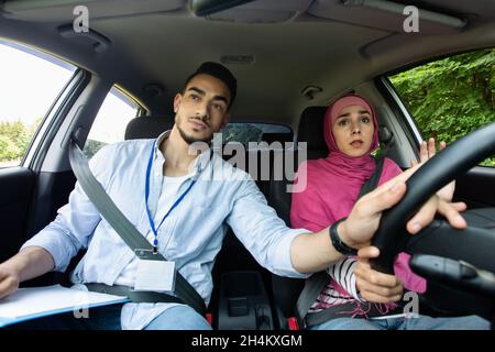 Nervous Muslim Lady In Hijab Mit Fahrstunde Mit Instruktor, Männlicher Lehrer Hilft Islamischen Weiblichen Studenten Auto Zu Fahren, Hält Lenkrad, Stockfoto