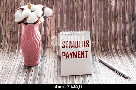 Der Stimulus Payment Incentive ist in einem Notizblock auf einem Holztisch neben einer Vase mit einer Baumwollblume in Vintage-Schrift geschrieben Stockfoto