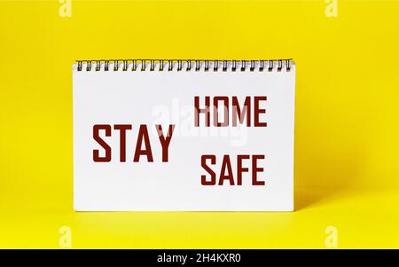 Worte Stay Home Stay Safe auf Notizblock und gelbem Hintergrund geschrieben. Self Quarantine at Home-Konzept zu Hause bleiben während einer Pandemie Stockfoto