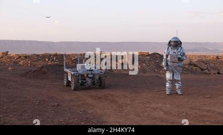 Ein analoger Astronaut, gekleidet in einen speziellen Raumanzügen, umläuft einen Rover auf dem Gelände der Mars-ähnlichen Forschungseinrichtung, die für die AMADEE-20-Mars-Simulation am Ramon-Krater in der Negev-Wüste in Israel gebaut wurde. Sechs Analogastronauten aus Israel, Portugal, Spanien, Deutschland, den Niederlanden und Österreich haben eine dreiwöchige Isolation innerhalb der Forschungseinrichtung abgeschlossen und konnten ihren Lebensraum nur in Raumanzügen verlassen. Das Team führte eine Reihe von wissenschaftlichen und technologischen Experimenten durch, in der Hoffnung, die Grundlagen für zukünftige bemannte Missionen zum Mars zu schaffen. Stockfoto