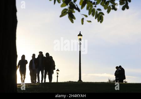 Silhouetten von Menschen, die den Herbstuntergang auf dem Gipfel des Primrose Hill im Norden Londons, Großbritannien, beobachten Stockfoto