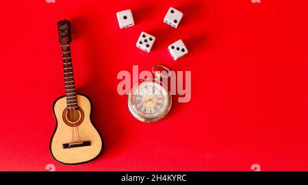 Gitarre, Würfel und Uhr auf rotem Hintergrund Stockfoto