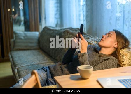 Frau benutzt ihr Telefon, das im Wohnzimmer auf der Couch oder dem Sofa liegt Stockfoto