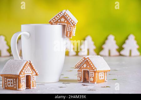 Lebkuchenhütten und eine Tasse Milch auf einer weißen Betonoberfläche mit Funkeln, Nahaufnahme. Weihnachtsfeier Konzept Stockfoto