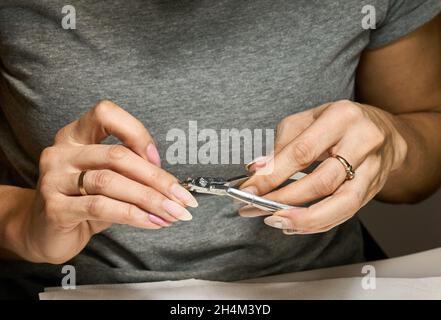 Frau macht Maniküre für sich mit Nagelknipser. Makro-Fotos in hoher Qualität. Stockfoto