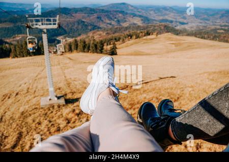 Seilbahn in den Herbstbergen. Beine in weißen Sneakers und schwarzen Stiefeln. Reise in die Berge. Freizeit Stockfoto