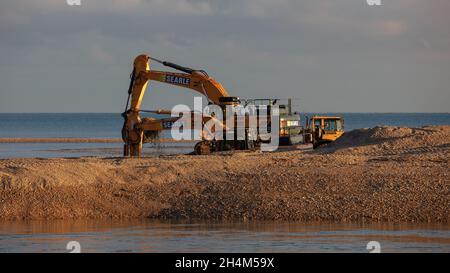 Pagham, Großbritannien. November 2021. Schwere Maschinen sahen Graben auf Pagham Schindelspieß, die Schaffung eines Kanals, die angenommen wird, um die Erosion am Strand in Pagham zu reduzieren, bedrohen in der Nähe Grundstücke. Quelle: Joe Kuis / Alamy Reportage Stockfoto