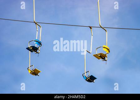 Leere Sessellifte hängen an einem Kabel auf einem Hintergrund von blauem Himmel Stockfoto