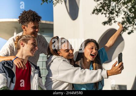 Eine Gruppe von glücklichen Teenagern, die auf der Straße in der Stadt am Telefon lachten. Stockfoto