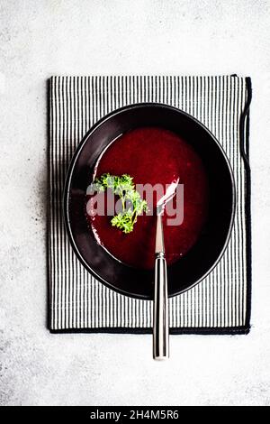 Gesunde Rote-Beete-Sahnesuppe, serviert in einer schwarzen Keramikschale auf rustikalem Hintergrund Stockfoto