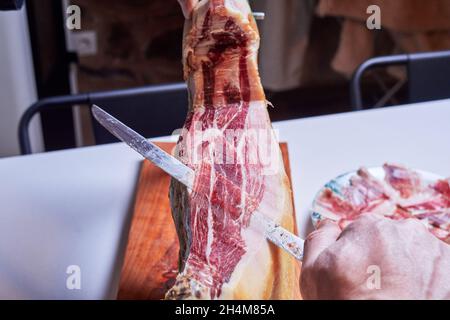 Hand eines professionellen Schinkenschneiders, der einen iberischen Schinken in dünne, verzehrfertige Scheiben schneidet Stockfoto