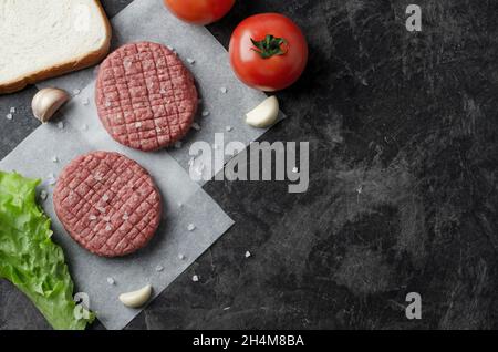 Rohe hausgemachte Grill-Rindfleisch-Burger mit Salat und Tomaten. Draufsicht und Platz für Text. Pfeffer und Salz auf Küchentisch Hintergrund. Stockfoto