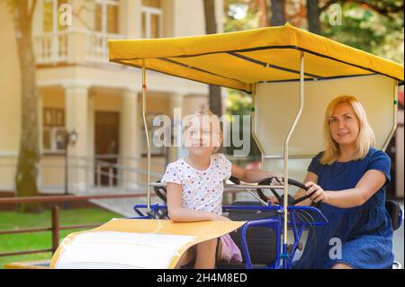 Eine schöne junge Frau in einem blauen Denim-Kleid mit einem kleinen Mädchen, das auf einem vier-Personen-Fahrrad sitzt. Palanga, Litauen, Ostsee, Stockfoto