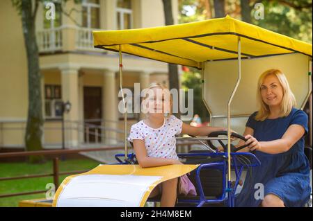 Eine schöne junge Frau in einem blauen Denim-Kleid mit einem kleinen Mädchen, das auf einem vier-Personen-Fahrrad sitzt. Palanga, Litauen, Ostsee, Stockfoto