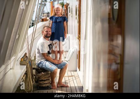 Ein kleines Mädchen sitzt in den Armen eines Mannes auf dem Deck eines großen Segelschiffs in der Stadt Klaipeda, Litauen Stockfoto