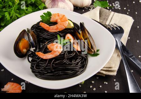 Schwarze Pasta mit Meeresfrüchten. Garnelen, Spaghetti, Basilikum, Knoblauch, Gewürze und Muscheln vor dunkler Grunge-Kulisse. Stockfoto