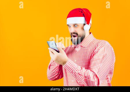 Bärtiger Mann mit Weihnachtshut der Weihnachtsmann schaut ins Telefon Stockfoto