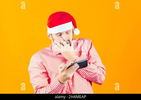 Ein Mann, der einen Weihnachtsmannhut trägt, sieht schockiert ins Telefon Stockfoto