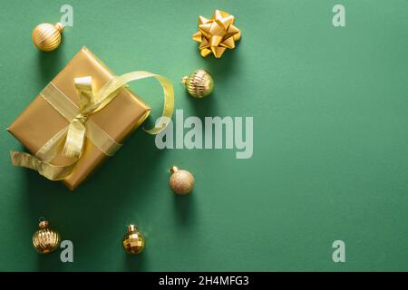 Weihnachtsgeschenk in Gold und Kugeln auf grünem Hintergrund. Draufsicht. Weihnachtsgrußkarte mit Kopierplatz. Stockfoto