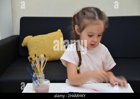 Ein altes Mädchen aus der Vorschule sitzt an einem Tisch und zeichnet mit bunten Farben und Pinsel. Kreativität von Kindern. Hobbys für Kinder niedliches Kind beschäftigt sich mit Crea Stockfoto