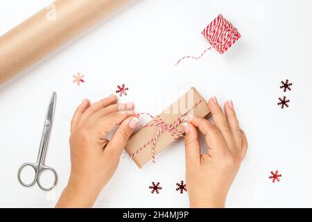 Flach legen weibliche Hände binden Schleife aus roten festlichen Seil auf Weihnachten Geschenkbox mit Dekor aus roten Schneeflocken auf weißem isolierten Hintergrund Stockfoto