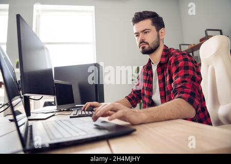 Foto von ernst fokussierten jungen Mann professionelle Programmierer Blick Bildschirm sitzen Schreibtisch drinnen im Büro Stockfoto