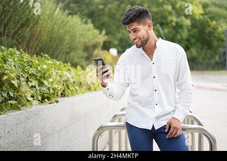Hübscher junger Mann mit gemischter Rasse, lächelnd, mit einem Mobiltelefon im Freien. Hochwertige Fotos Stockfoto