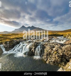 Ein Wasserfall auf dem Allt Dearg Mor Fluss mit den Black Cuillin Bergen in der Ferne mit Wolkenbank darüber, Sligachan, Isle of Skye, Schottland, Großbritannien Stockfoto