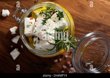 In Olivenöl marinierter Feta-Käse mit frischen Kräutern im Glasgefäß. Draufsicht Stockfoto