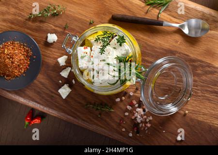 In Olivenöl marinierter Feta-Käse mit frischen Kräutern im Glasgefäß. Draufsicht Stockfoto
