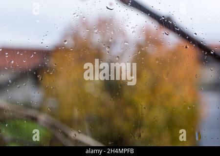 Regentropfen fallen auf das Fenster und verschwommener Hintergrund an einem regnerischen Herbsttag. Wetter- und Saisonkonzept. Nahaufnahme, selektiver Fokus Stockfoto