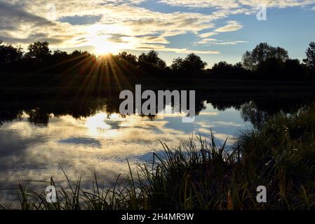 Friedlicher Sonnenuntergang über reflektierender ruhiger Wasseroberfläche mit Bäumen in Silhouette Stockfoto