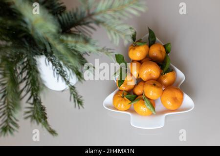 Kleine reife Mandarinen mit Blättern, auf Teller in Form von Weihnachtsbaum auf beigem Hintergrund. Konzept Winter Vitaminfutter. Moody Still Life festliche Komp Stockfoto