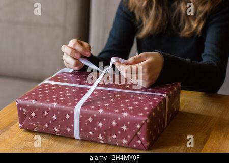 Mädchen bindet eine Schleife auf einem Weihnachtsgeschenk Stockfoto