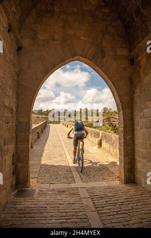 Pilger, die über die mittelalterliche Brücke Puente Romanico in der spanischen Stadt Puente la Reina radeln, während sie auf der Pilgerroute Camino de Santiago reiten Stockfoto