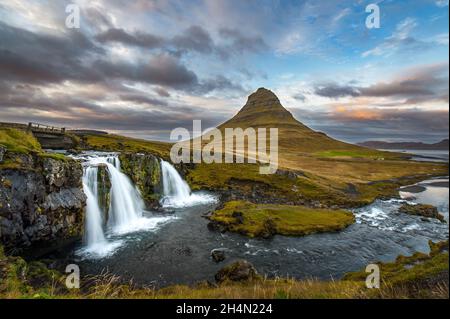 Ein Wasserfall (Kirkjufellfoss) und Fluss vor einem Berg (Kirkjufell) und Sonnenuntergang in Island Stockfoto