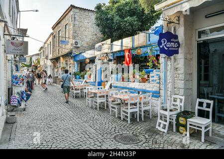 Alacati, Izmir, Türkei – 3. Oktober 2020. Eine schmale gepflasterte Straße in Alacati Resort Stadt der Provinz Izmir in der Türkei. Blick mit Menschen, Stein Hou Stockfoto