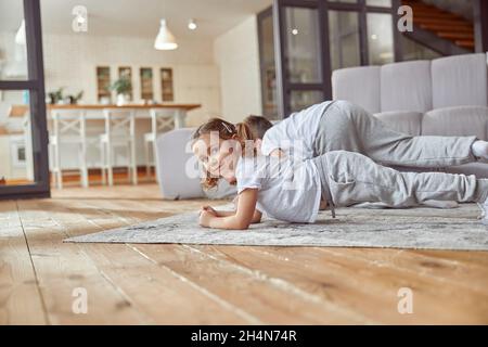 Fröhliches kleines Mädchen macht Training mit der Familie zu Hause Stockfoto