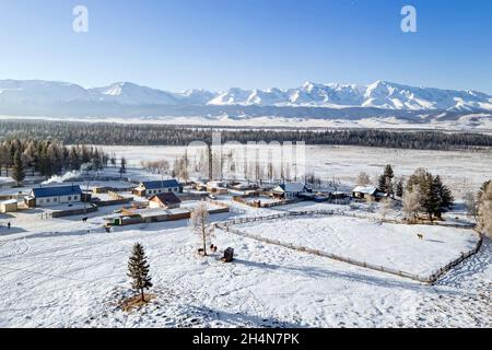 Russisches Dorf. Schöne ländliche Landschaft im Winter. Holzhaus auf dem Hintergrund der Berge. Feld für Walking Rinder Weide und vegeta Stockfoto