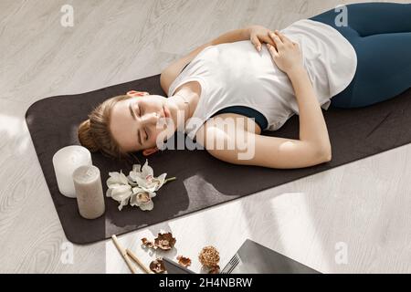 Junge schöne sportliche blonde Mädchen ist in Hatha Yoga in einem modernen Licht Studio engagiert. Sie liegt auf dem Boden und meditiert mit geschlossenen Augen. Schließen- Stockfoto