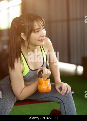 Junge asiatische Frau genießen das Training mit dem Heben Wasserkocher Glocke mit einer Hand in der Turnhalle. Sport Bodybuilding Konzept Stockfoto