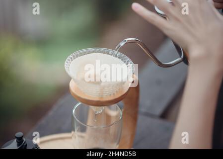 Tropfen Sie Kaffee von Hand, und Barista gießt das heiße Wasser in den Filter, bevor Sie die Kaffeebohnen gießen. Stockfoto