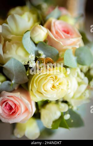 Eheringe auf einem Rosenblatt. Konzept für eine Hochzeitskarte. Der Blumenstrauß der Braut. Stockfoto