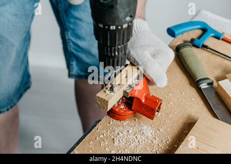 Professioneller Arbeiter, der Elektrogeräte hält und ein Loch in ein Holzbrett bohrt. Haus Renovierung und Verbesserung Konzept. DIY. Stockfoto