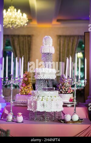 Weiße dreistufige Hochzeitstorte mit cremefarbenen Blumen auf einem Ständer dekoriert. Stockfoto