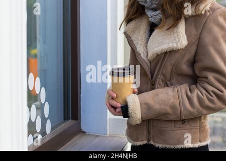 Mädchen in einem braunen Mantel steht auf der Straße mit Kaffee zum Mitnehmen Stockfoto