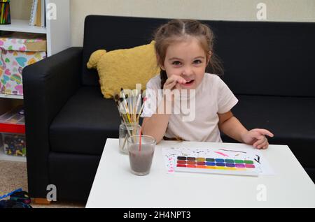 Ein altes Mädchen aus der Vorschule sitzt an einem Tisch und zeichnet mit bunten Farben und Pinsel. Kreativität von Kindern. Hobbys für Kinder niedliches Kind beschäftigt sich mit Crea Stockfoto