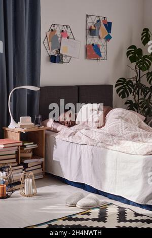 Afrikanische junge Frau, die sich auf dem Bett entspannt und in ihrem modernen Schlafzimmer schläft Stockfoto