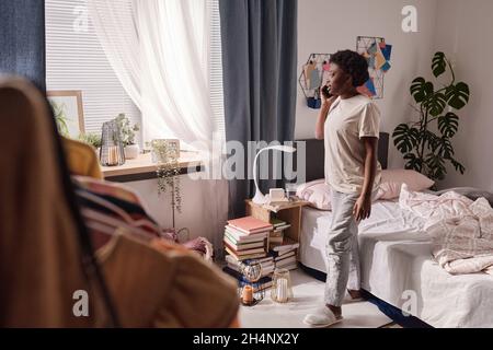 Afrikanische junge Frau, die auf ihrem Handy spricht, während sie um ihr Schlafzimmer geht Stockfoto